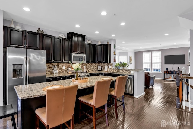 kitchen with dark wood-type flooring, a kitchen island with sink, tasteful backsplash, open floor plan, and stainless steel appliances