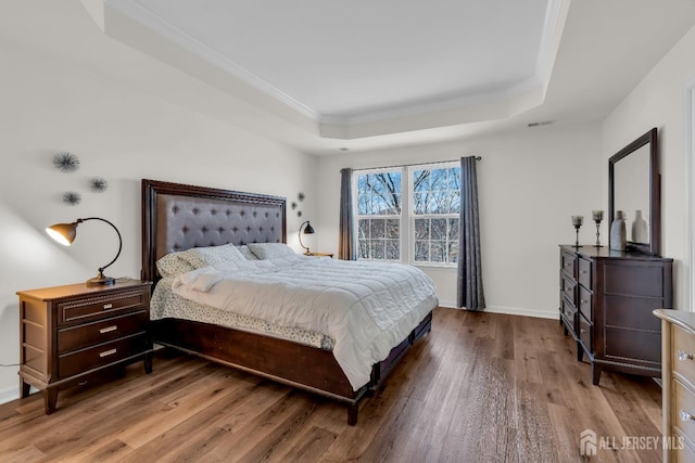 bedroom with visible vents, wood finished floors, baseboards, crown molding, and a raised ceiling