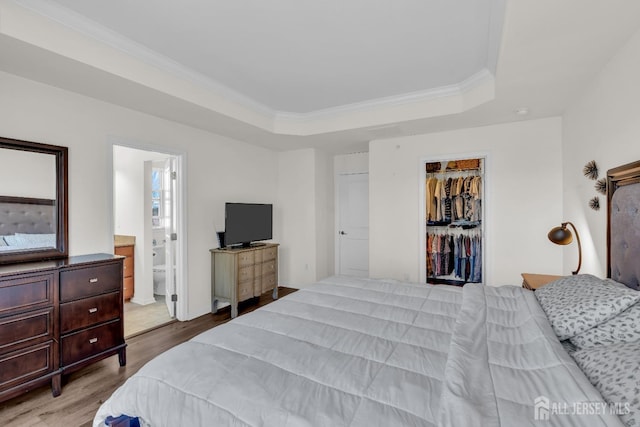 bedroom featuring ensuite bathroom, wood finished floors, crown molding, a raised ceiling, and a spacious closet