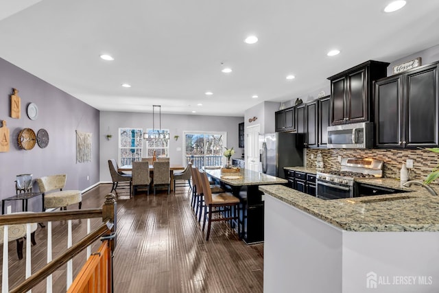 kitchen featuring a sink, backsplash, light stone countertops, appliances with stainless steel finishes, and dark cabinets