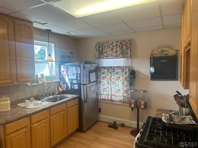 kitchen featuring a drop ceiling, light wood-style flooring, a sink, backsplash, and freestanding refrigerator