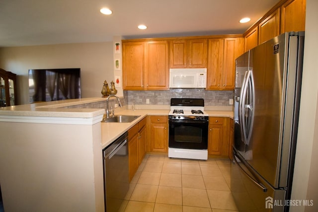 kitchen featuring light tile patterned floors, a peninsula, a sink, stainless steel appliances, and backsplash