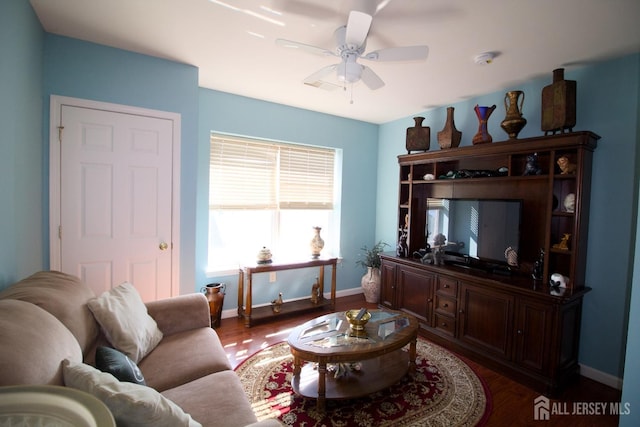 living area with baseboards, a ceiling fan, and dark wood-style flooring