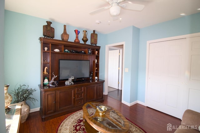 living room with baseboards, a ceiling fan, and dark wood-style flooring