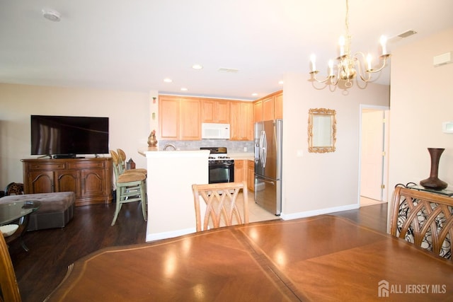 kitchen with gas stove, white microwave, light brown cabinets, stainless steel fridge, and a chandelier