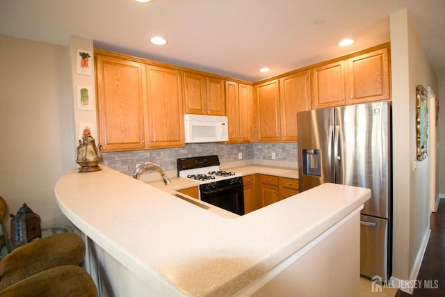 kitchen featuring a peninsula, white microwave, stainless steel fridge, tasteful backsplash, and gas stove