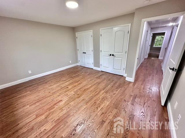 unfurnished bedroom with hardwood / wood-style flooring and multiple closets