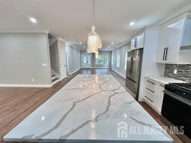 kitchen featuring range with gas cooktop, light stone counters, decorative light fixtures, stainless steel refrigerator, and white cabinets