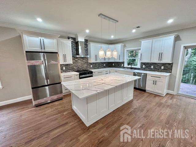 kitchen with wall chimney exhaust hood, white cabinetry, decorative light fixtures, a center island, and stainless steel appliances