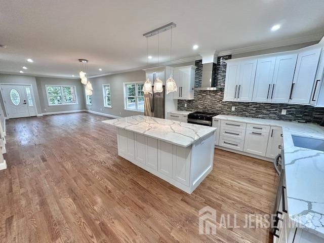 kitchen with light stone counters, decorative light fixtures, a kitchen island, wall chimney range hood, and white cabinets