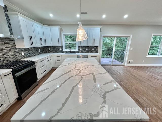 kitchen featuring range with gas cooktop, white cabinets, hanging light fixtures, light stone countertops, and wall chimney range hood