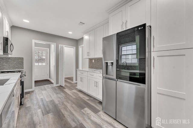 kitchen with light wood-type flooring, stainless steel appliances, white cabinets, light stone countertops, and tasteful backsplash