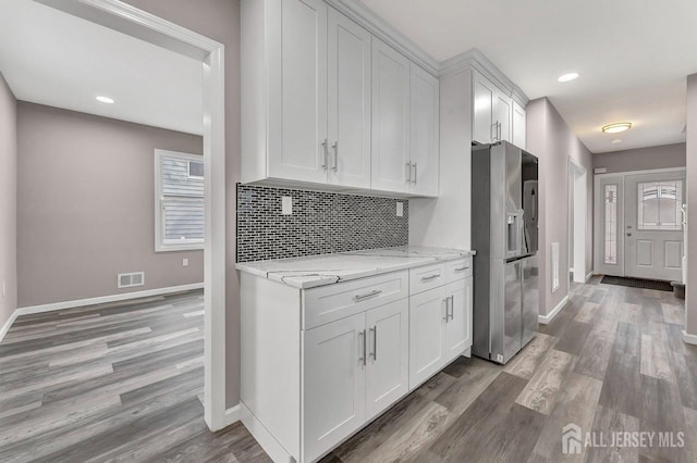 kitchen featuring white cabinetry, stainless steel fridge with ice dispenser, backsplash, light stone counters, and wood-type flooring