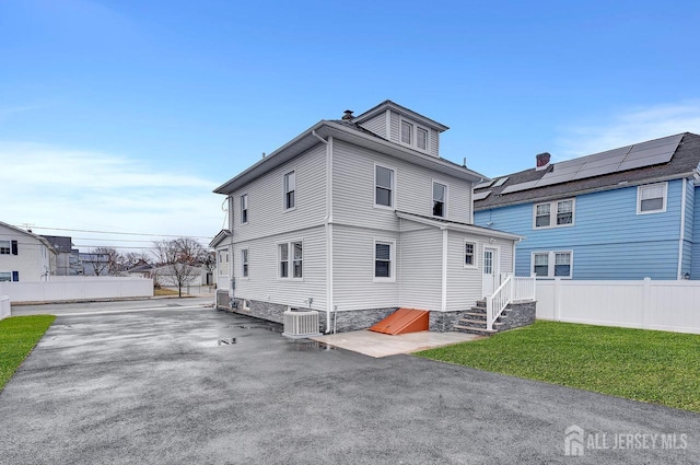 back of property featuring central AC, solar panels, and a yard