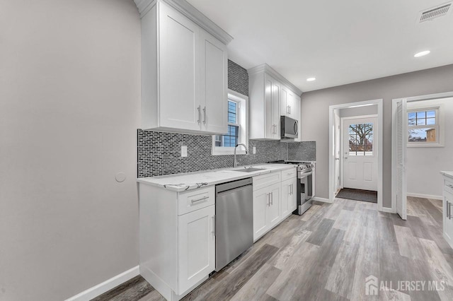 kitchen featuring tasteful backsplash, stainless steel appliances, white cabinets, light hardwood / wood-style floors, and sink