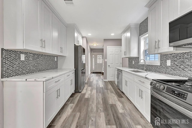 kitchen with white cabinetry, light wood-type flooring, sink, light stone counters, and appliances with stainless steel finishes