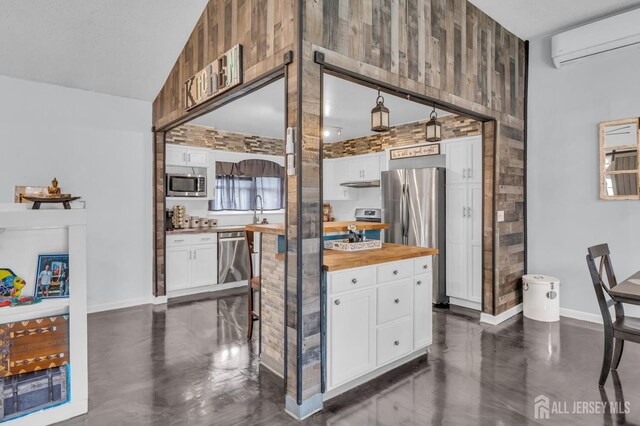 kitchen with a wall unit AC, stainless steel appliances, wood counters, wooden walls, and white cabinetry