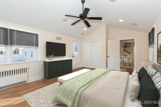 bedroom with vaulted ceiling, radiator heating unit, ceiling fan, light wood-type flooring, and a closet