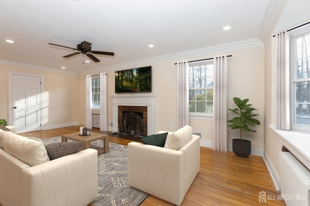 living room with ceiling fan, a brick fireplace, radiator, and light wood-type flooring