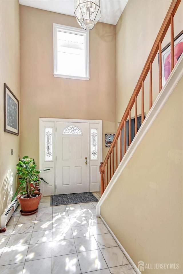 entrance foyer with stairway, a baseboard radiator, a towering ceiling, and a chandelier