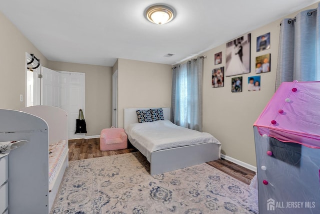 bedroom with baseboards, visible vents, and wood finished floors