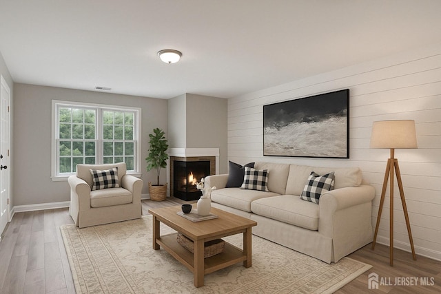 living room featuring wood finished floors, visible vents, a multi sided fireplace, and baseboards
