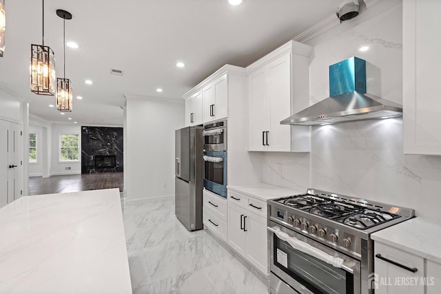 kitchen featuring white cabinetry, wall chimney exhaust hood, light stone counters, decorative light fixtures, and appliances with stainless steel finishes