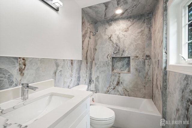 full bathroom featuring vanity, tiled shower / bath combo, a healthy amount of sunlight, tile walls, and toilet