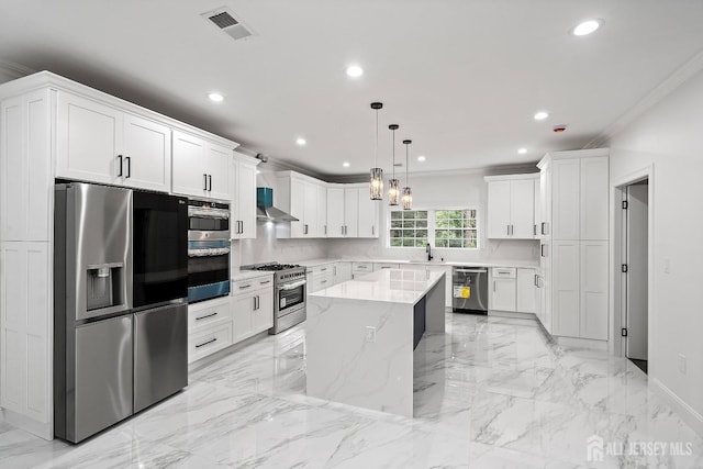 kitchen featuring wall chimney exhaust hood, stainless steel appliances, a center island, white cabinetry, and hanging light fixtures