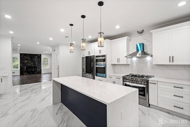 kitchen featuring a center island, white cabinets, wall chimney exhaust hood, appliances with stainless steel finishes, and decorative light fixtures