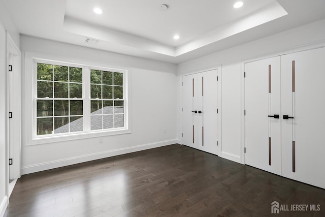 unfurnished bedroom with a raised ceiling, dark wood-type flooring, and two closets