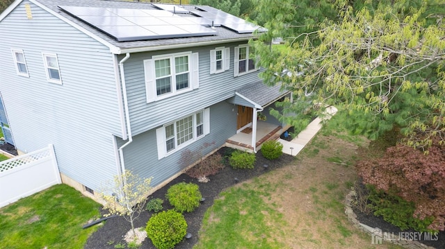 view of property exterior with fence, roof mounted solar panels, and roof with shingles