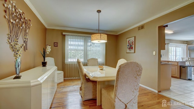 dining space with light wood finished floors, crown molding, and baseboards