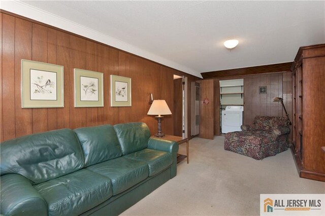 living room with washer / clothes dryer, light colored carpet, ornamental molding, and wood walls