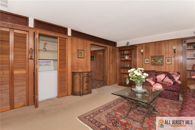 living room featuring washer / clothes dryer, light carpet, and wood walls