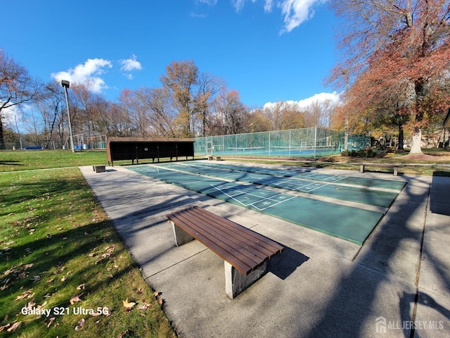 view of community with shuffleboard, fence, and a yard