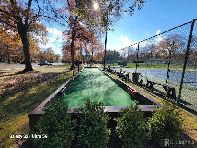 view of property's community with a tennis court and fence