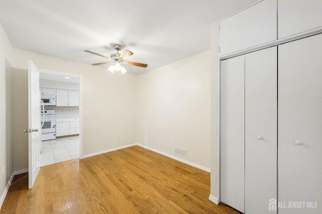 unfurnished bedroom featuring light wood finished floors, baseboards, visible vents, ceiling fan, and a closet