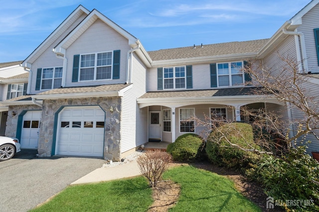 view of front of property with an attached garage, a porch, roof with shingles, stone siding, and driveway