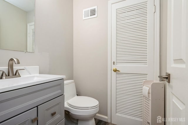 half bath with visible vents, toilet, and vanity