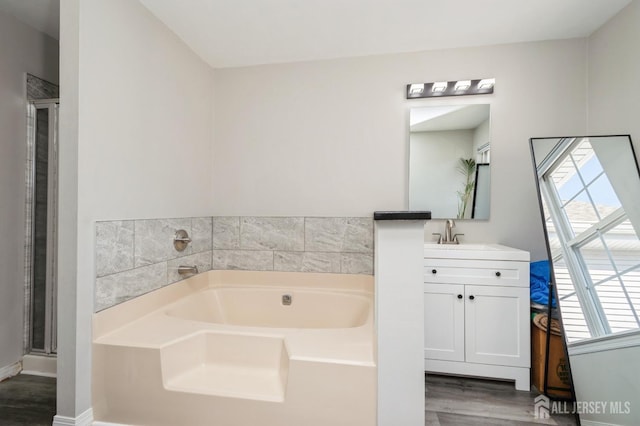 full bathroom featuring wood finished floors, a shower stall, baseboards, a bath, and vanity