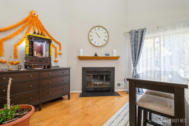 living room featuring light wood finished floors, baseboards, visible vents, and a fireplace with flush hearth