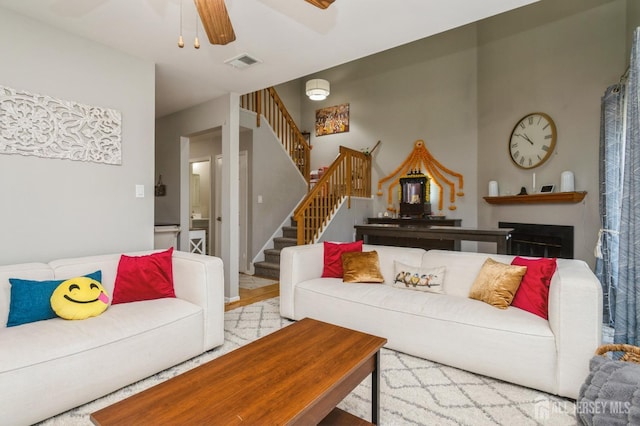 living area with visible vents, a fireplace, stairway, and a ceiling fan