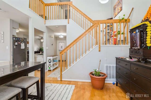 staircase with a towering ceiling, visible vents, wood finished floors, and a ceiling fan