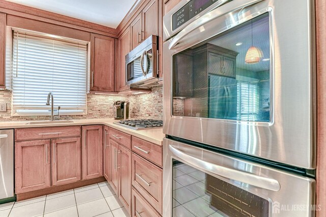 kitchen featuring pendant lighting, decorative backsplash, appliances with stainless steel finishes, light tile patterned flooring, and sink