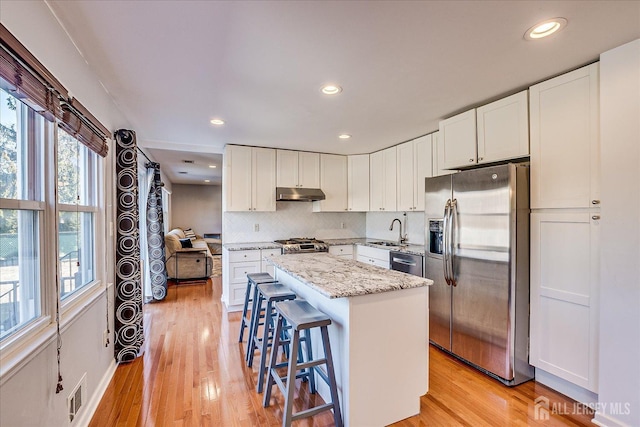 kitchen featuring visible vents, under cabinet range hood, a kitchen island, appliances with stainless steel finishes, and decorative backsplash