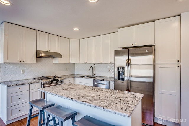 kitchen with under cabinet range hood, light stone counters, appliances with stainless steel finishes, white cabinets, and a sink