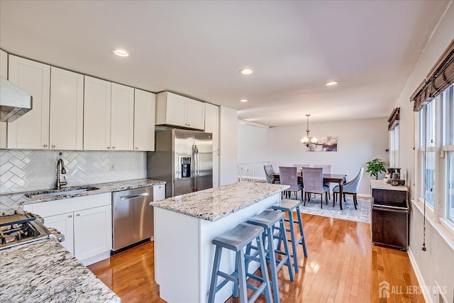 kitchen with light wood-style flooring, light stone counters, appliances with stainless steel finishes, white cabinets, and decorative backsplash