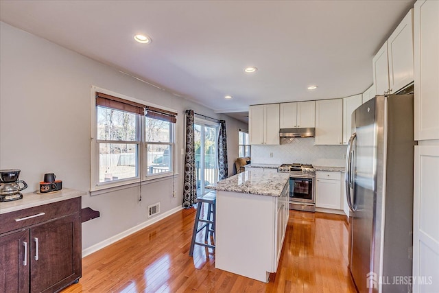 kitchen featuring visible vents, under cabinet range hood, tasteful backsplash, a center island, and appliances with stainless steel finishes