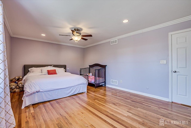 bedroom featuring baseboards, visible vents, light wood finished floors, and ornamental molding